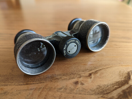 A pair of opera glasses on a table. Glasses are labeled "Hugo Wolf, Optiker, Wien I"