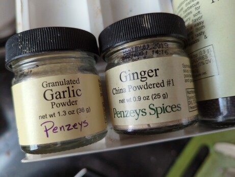 Jars of garlic powder and ginger next to each other on a spice rack