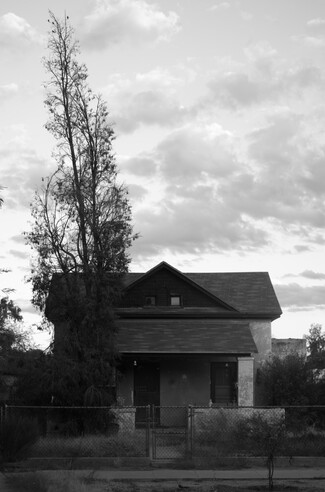 A house against a cloudy sky. A tall, barren tree looms beside. 