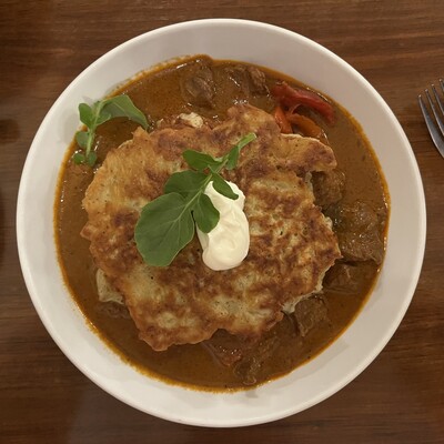 Potato pancakes stacked in a shallow sea of beef stew with red bell peppers. Perfect rainy day fare. 